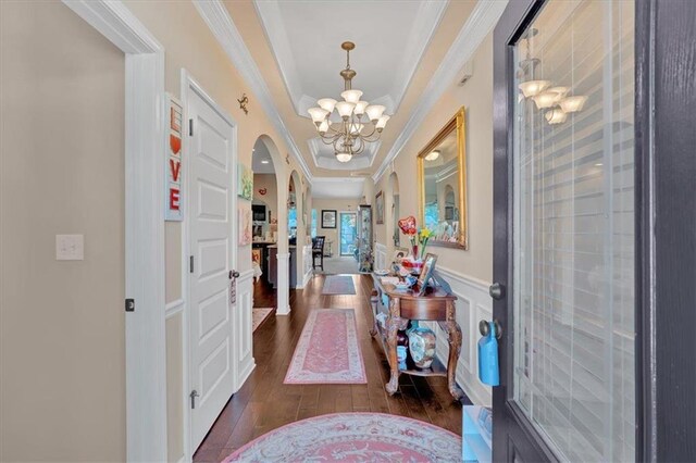 interior space featuring dark wood-type flooring, a notable chandelier, a raised ceiling, and ornamental molding