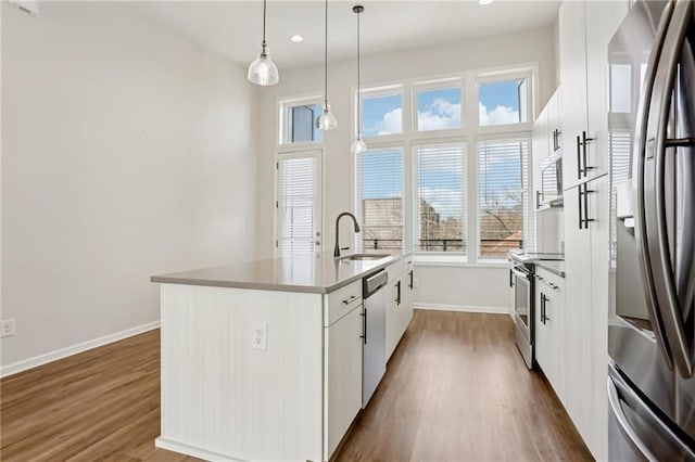 kitchen featuring appliances with stainless steel finishes, white cabinetry, sink, hanging light fixtures, and a kitchen island with sink