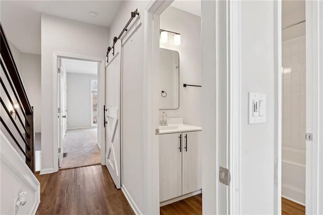 corridor featuring a barn door, dark wood-type flooring, and sink