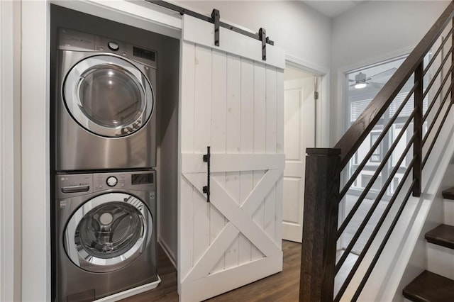 washroom with stacked washer and dryer, dark wood-type flooring, a barn door, and ceiling fan