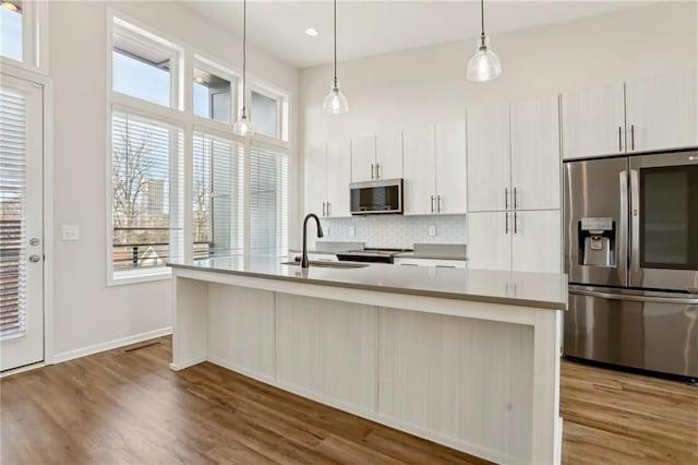 kitchen with appliances with stainless steel finishes, tasteful backsplash, a kitchen island with sink, decorative light fixtures, and sink