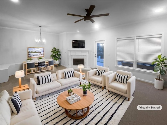 living room with baseboards, recessed lighting, a fireplace, ornamental molding, and ceiling fan with notable chandelier