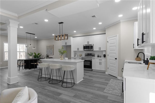 kitchen featuring a sink, white cabinets, appliances with stainless steel finishes, a center island, and decorative columns