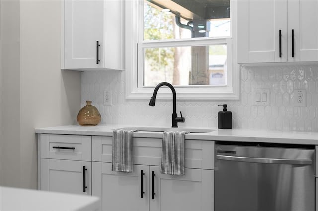 kitchen with white cabinets, backsplash, light countertops, and stainless steel dishwasher