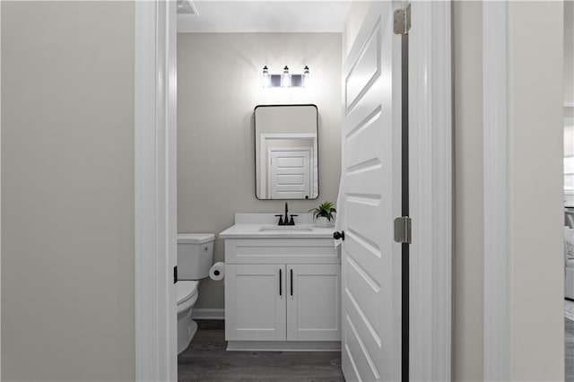 half bathroom featuring visible vents, vanity, wood finished floors, and toilet