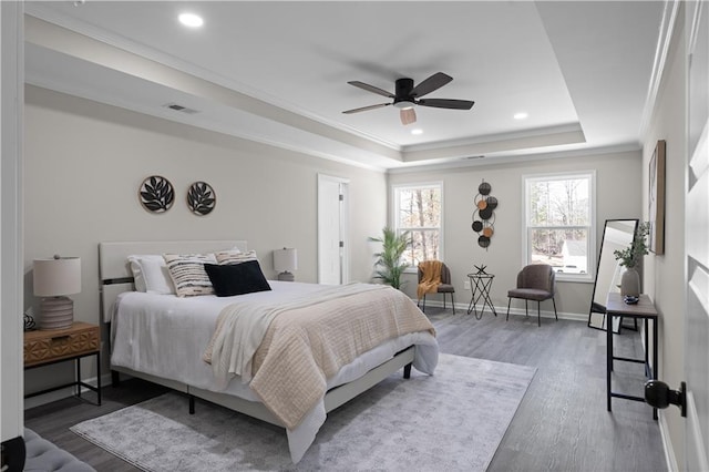 bedroom with wood finished floors, visible vents, baseboards, ornamental molding, and a tray ceiling