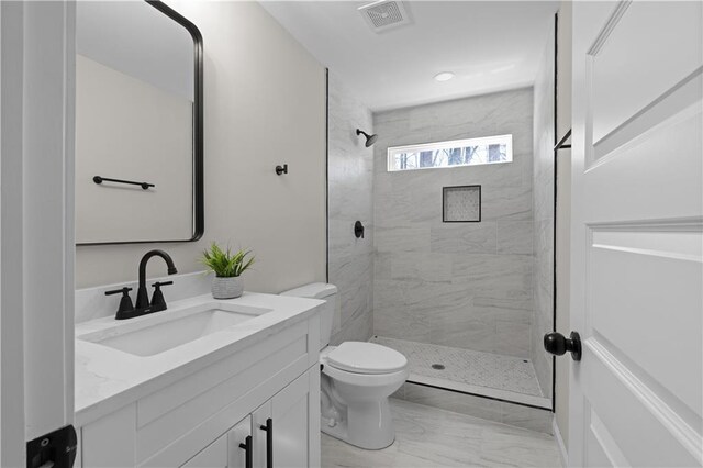 bathroom featuring marble finish floor, visible vents, a tile shower, and vanity