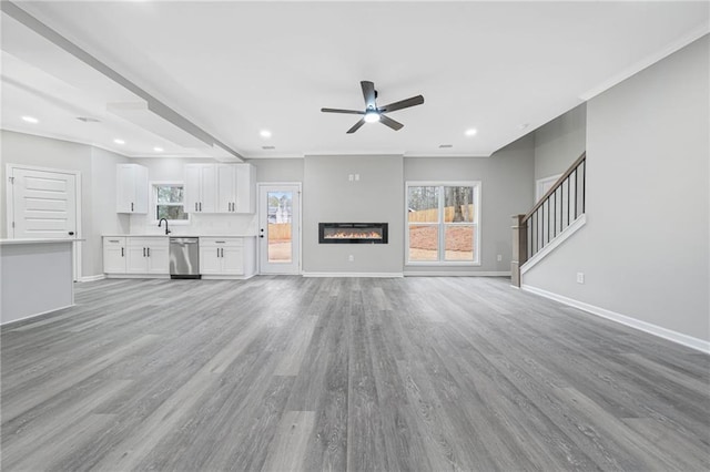 unfurnished living room with baseboards, a glass covered fireplace, light wood-style flooring, a sink, and recessed lighting