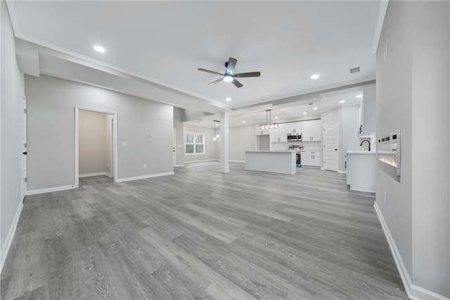 unfurnished living room featuring ceiling fan with notable chandelier, light wood-type flooring, baseboards, and recessed lighting