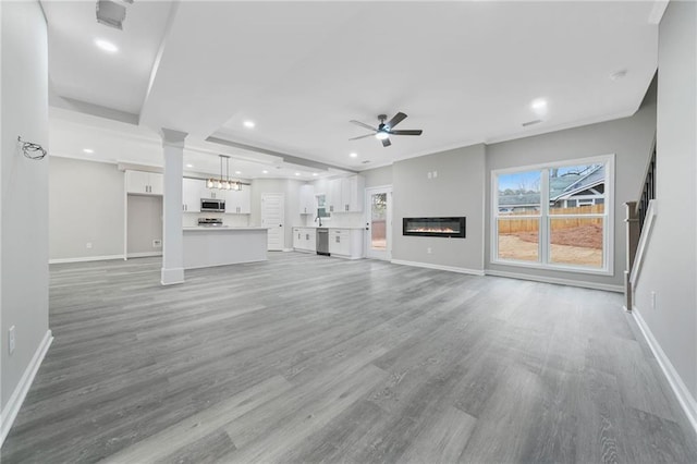 unfurnished living room with recessed lighting, light wood-style flooring, a glass covered fireplace, ceiling fan, and baseboards