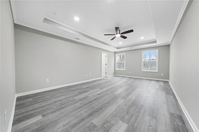 empty room featuring a tray ceiling, crown molding, recessed lighting, wood finished floors, and baseboards