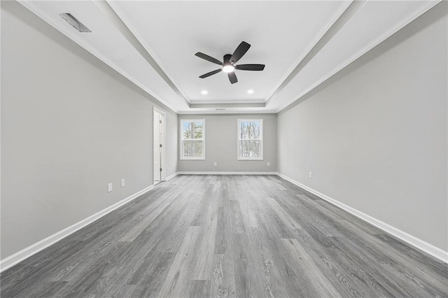 unfurnished room featuring a tray ceiling, recessed lighting, wood finished floors, and baseboards