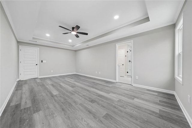 empty room featuring baseboards, a tray ceiling, crown molding, and wood finished floors