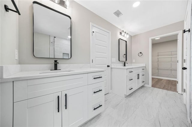 bathroom featuring marble finish floor, a spacious closet, two vanities, and a sink