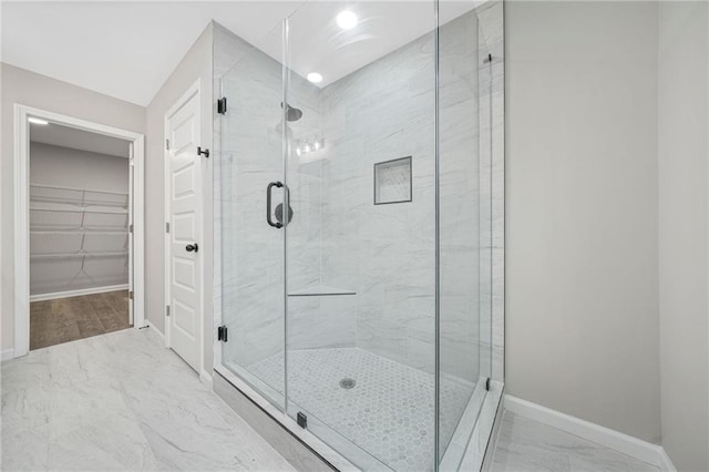 full bath with marble finish floor, a spacious closet, baseboards, and a stall shower