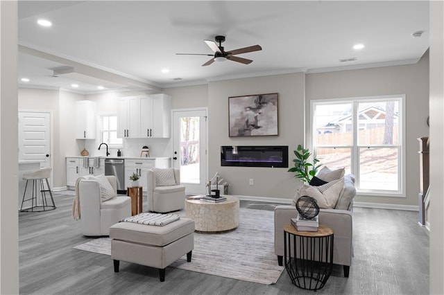 living room featuring ornamental molding, a glass covered fireplace, visible vents, and baseboards