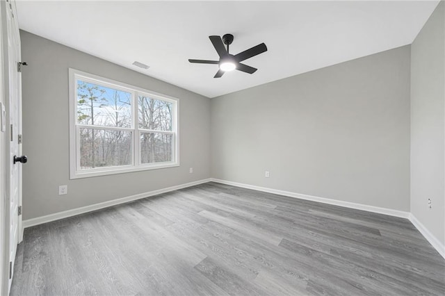 empty room with ceiling fan, visible vents, baseboards, and wood finished floors