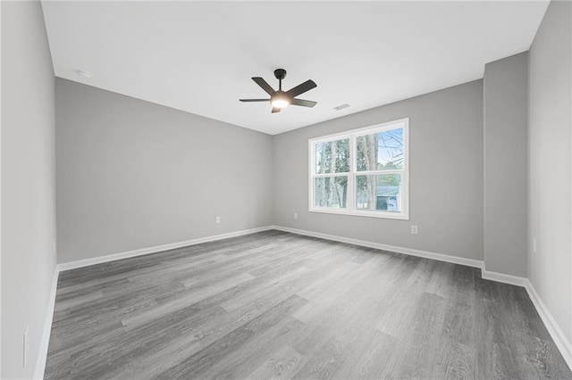 empty room featuring ceiling fan, wood finished floors, visible vents, and baseboards