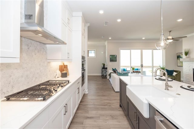 kitchen with stainless steel appliances, white cabinets, wall chimney range hood, ornamental molding, and tasteful backsplash