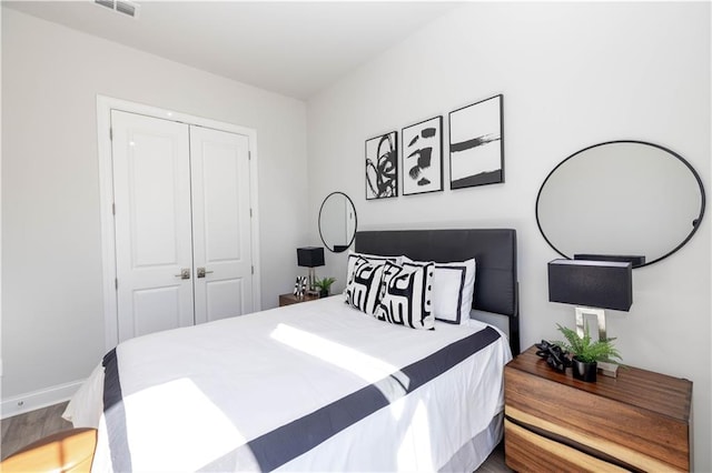 bedroom with baseboards, visible vents, a closet, and wood finished floors