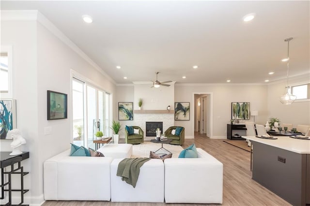 living area featuring baseboards, crown molding, a stone fireplace, light wood-style floors, and recessed lighting