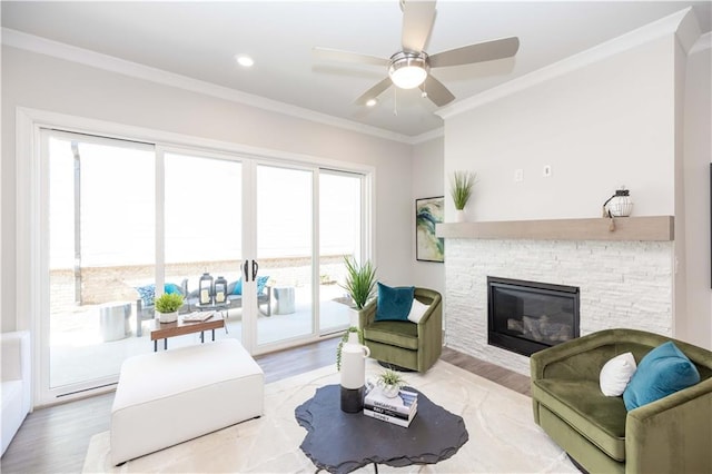 living area with ceiling fan, a stone fireplace, recessed lighting, wood finished floors, and crown molding