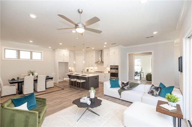 living area featuring recessed lighting, plenty of natural light, light wood-style flooring, and crown molding