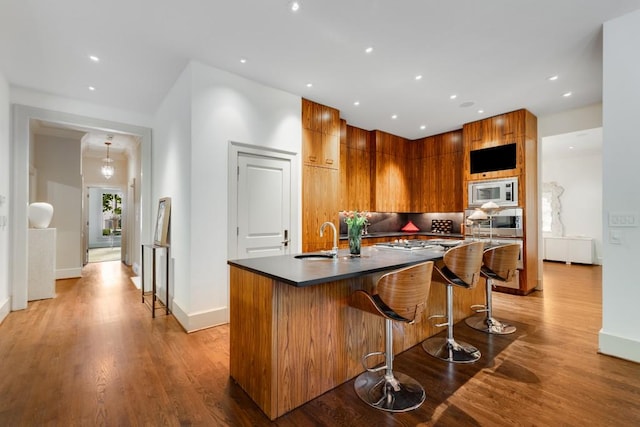 kitchen featuring stainless steel microwave, a center island with sink, sink, light hardwood / wood-style flooring, and a kitchen bar