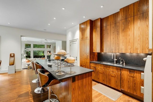 kitchen featuring a kitchen breakfast bar, sink, light hardwood / wood-style flooring, ceiling fan, and tasteful backsplash