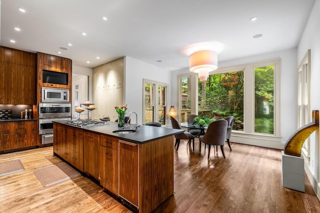 kitchen featuring light wood-type flooring, stainless steel appliances, a kitchen island with sink, and sink