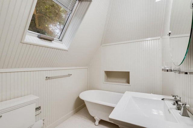 bathroom featuring toilet, sink, lofted ceiling with skylight, and a tub to relax in