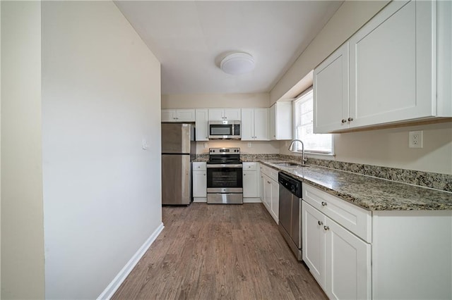 kitchen with sink, dark stone countertops, stainless steel appliances, light hardwood / wood-style floors, and white cabinets