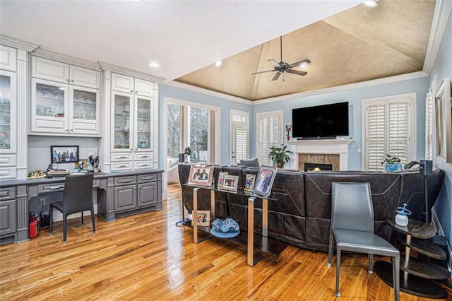 interior space with crown molding, a fireplace, built in desk, light wood-style floors, and vaulted ceiling