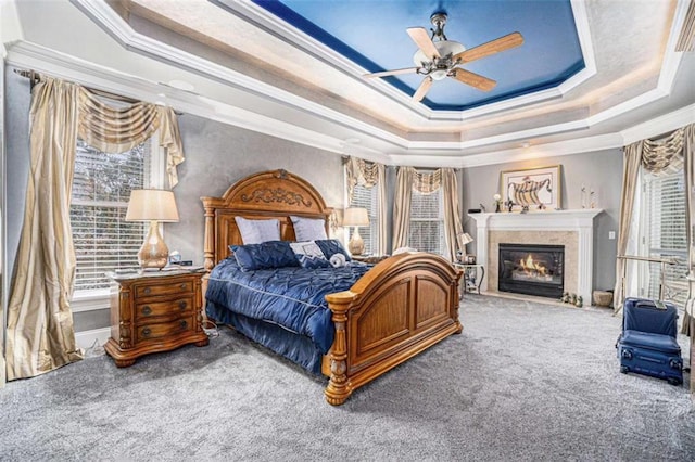 carpeted bedroom featuring ceiling fan, a raised ceiling, crown molding, and a glass covered fireplace