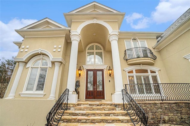 view of exterior entry featuring french doors, a balcony, and stucco siding