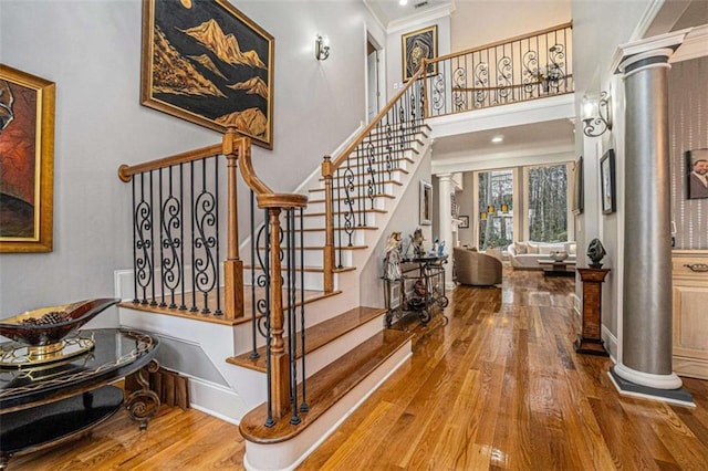 stairs with ornamental molding, a high ceiling, ornate columns, and wood finished floors