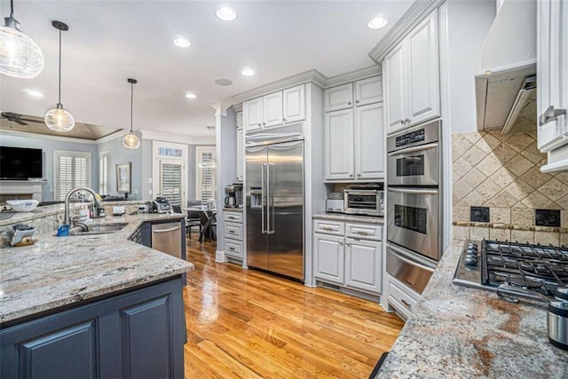 kitchen featuring white cabinets, appliances with stainless steel finishes, open floor plan, a sink, and a warming drawer