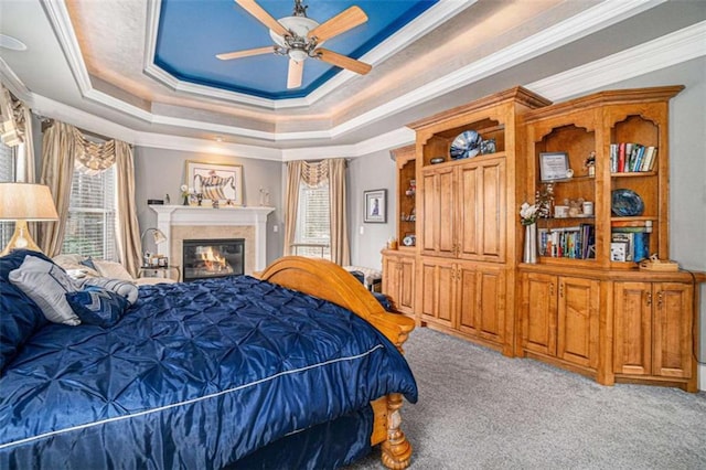 carpeted bedroom with a glass covered fireplace, a raised ceiling, and crown molding