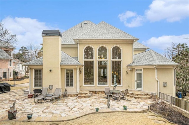 back of property featuring a patio area, roof with shingles, a chimney, and stucco siding