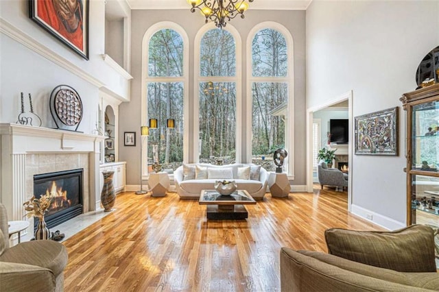 living room featuring a notable chandelier, wood-type flooring, ornamental molding, and a tiled fireplace