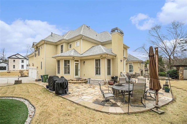 back of house with a chimney, roof with shingles, an attached garage, a patio area, and stucco siding