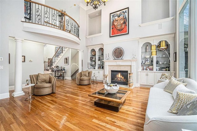 living area featuring built in features, a glass covered fireplace, wood finished floors, ornate columns, and stairs