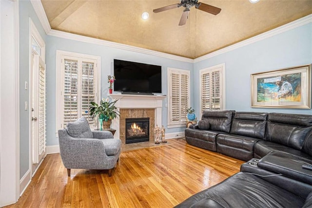 living area featuring baseboards, hardwood / wood-style flooring, a fireplace with flush hearth, ornamental molding, and vaulted ceiling