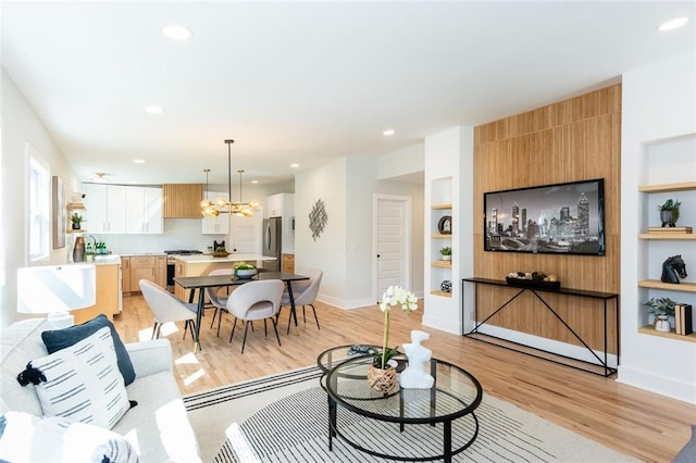 living area with built in shelves, baseboards, light wood-style flooring, recessed lighting, and a notable chandelier