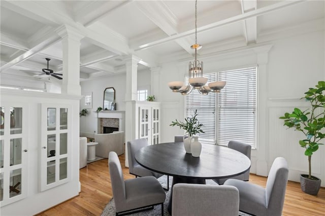 dining area featuring ceiling fan with notable chandelier, a wealth of natural light, light hardwood / wood-style floors, and ornate columns