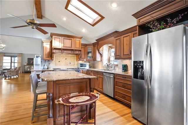 kitchen featuring a center island, brown cabinets, appliances with stainless steel finishes, glass insert cabinets, and a kitchen breakfast bar