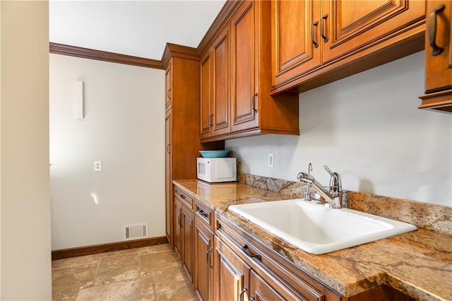 kitchen with visible vents, white microwave, brown cabinetry, a sink, and baseboards