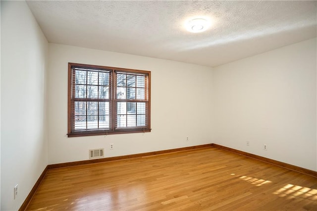 spare room with a textured ceiling, visible vents, and wood finished floors