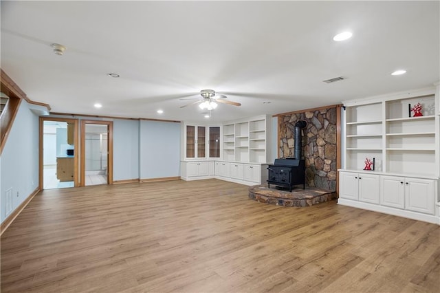 unfurnished living room featuring visible vents, a ceiling fan, a wood stove, light wood-type flooring, and baseboards