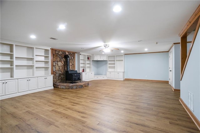 unfurnished living room with a wood stove, a ceiling fan, baseboards, and wood finished floors